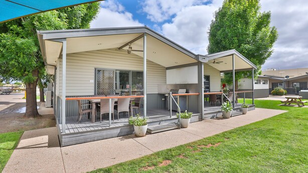 A mobile home with a covered porch, outdoor seating, and potted plants.