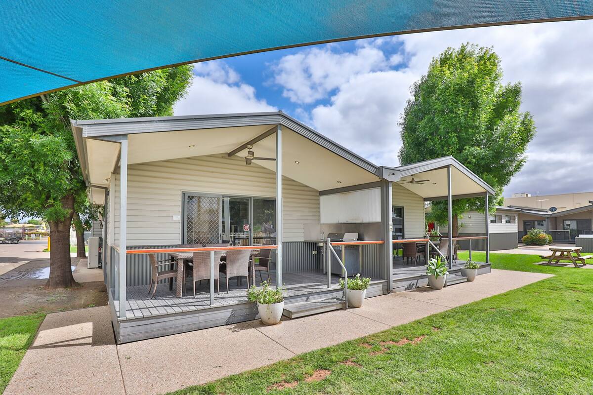 A mobile home with a covered porch, outdoor seating, and potted plants.