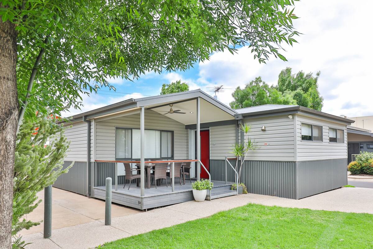 A single-story motel with a covered patio, a red door, and a small garden area.