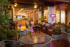 An indoor seating area with wicker furniture, a bar in the background, and a neon sign. - Karon Sunshine Guesthouse & Bar (Karon)