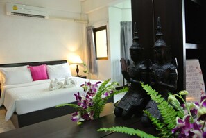 A hotel room with a bed, pillows, a nightstand, a lamp, a statue, and a sign. - Karon Sunshine Guesthouse & Bar (Karon)