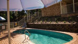 A swimming pool with a tiled deck, a metal ladder, and a covered area with a white umbrella. - Golf Club Motor Inn Wingham (Wingham)