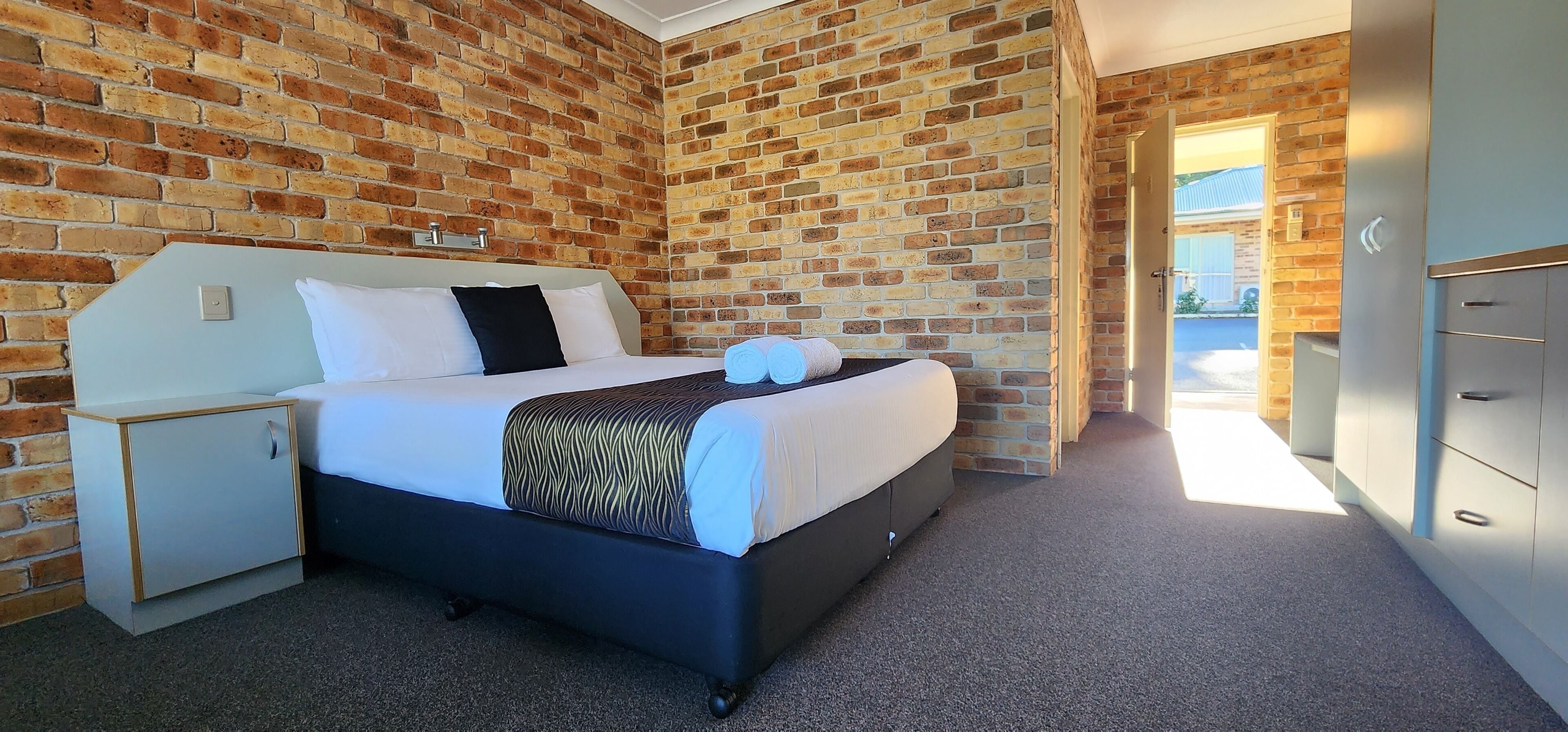 Ein Hotelzimmer mit Backsteinwand, einem Bett mit weißer Bettwäsche, einem kleinen Nachttisch und einem Kleiderschrank.