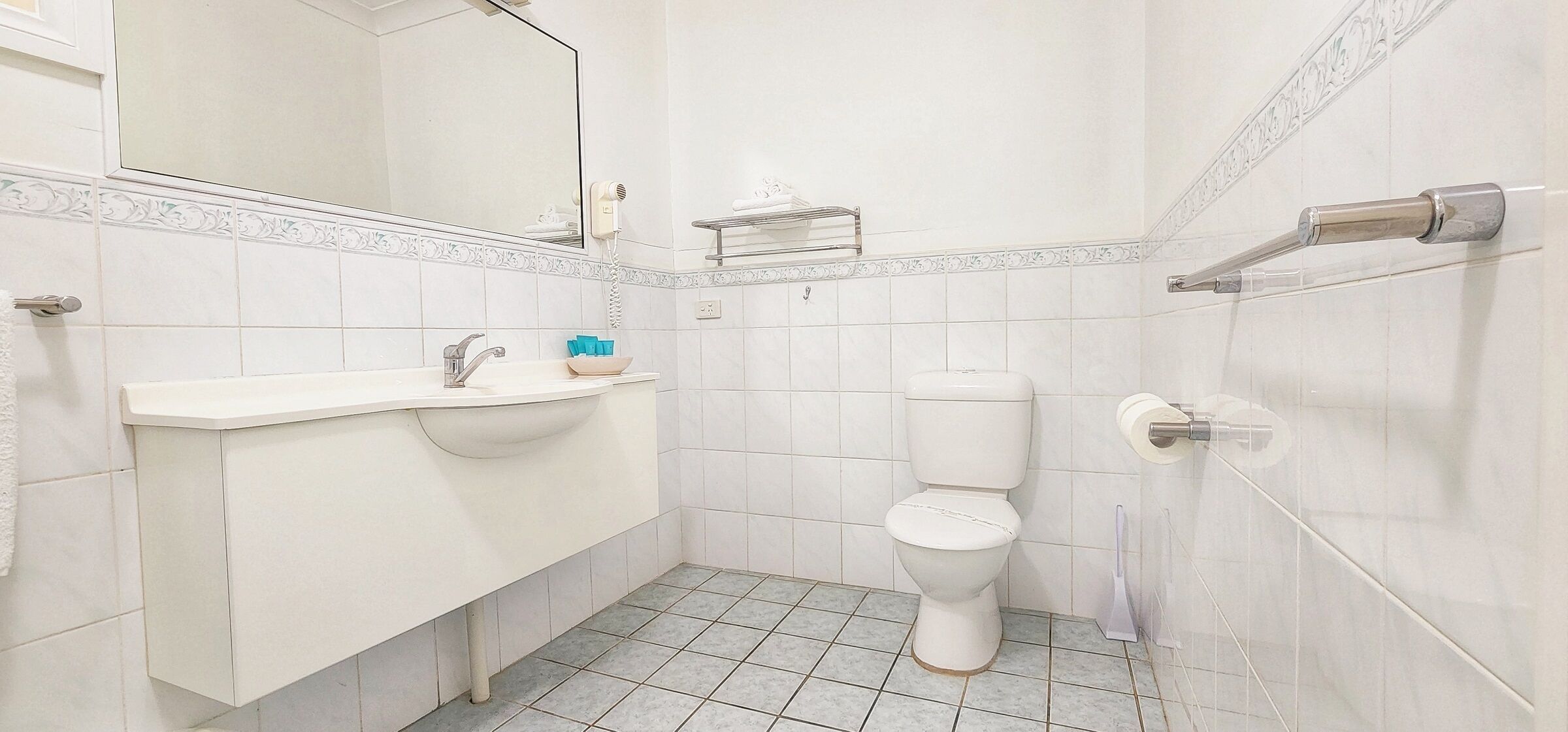 A bathroom with a white sink, a toilet, a mirror, and a towel rack.
