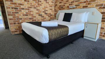 A single bed with a black frame and white bedding, a small white cabinet, and a brick wall.