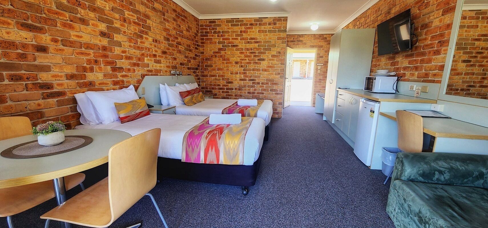 Une chambre d’hôtel compacte avec un mur en briques, deux lits, une petite kitchenette et un coin salon.