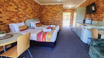 Une chambre d’hôtel compacte avec un mur en briques, deux lits, une petite kitchenette et un coin salon.