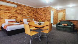 A hotel room with brick walls, two beds, a dining table with chairs, and a green sofa. - Golf Club Motor Inn Wingham (Wingham)