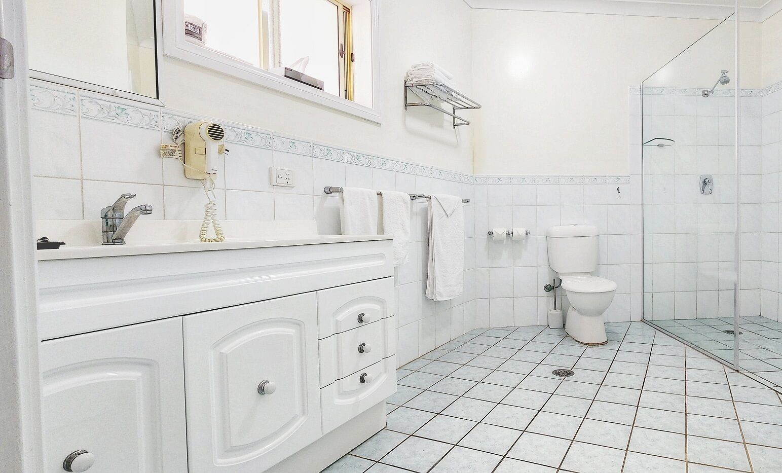 Baño con lavamanos, tocador, inodoro, zona de ducha y perchero para toallas.