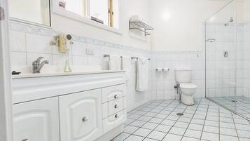 Baño con lavamanos, tocador, inodoro, zona de ducha y perchero para toallas.