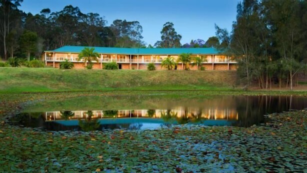 A hotel with a green roof, multiple balconies, and a reflection in a pond surrounded by lily pads. - Golf Club Motor Inn Wingham (Wingham)