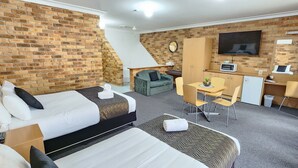 A hotel room with a brick wall, a bed, a desk, a chair, a TV, and a small kitchenette. - Golf Club Motor Inn Wingham (Wingham)