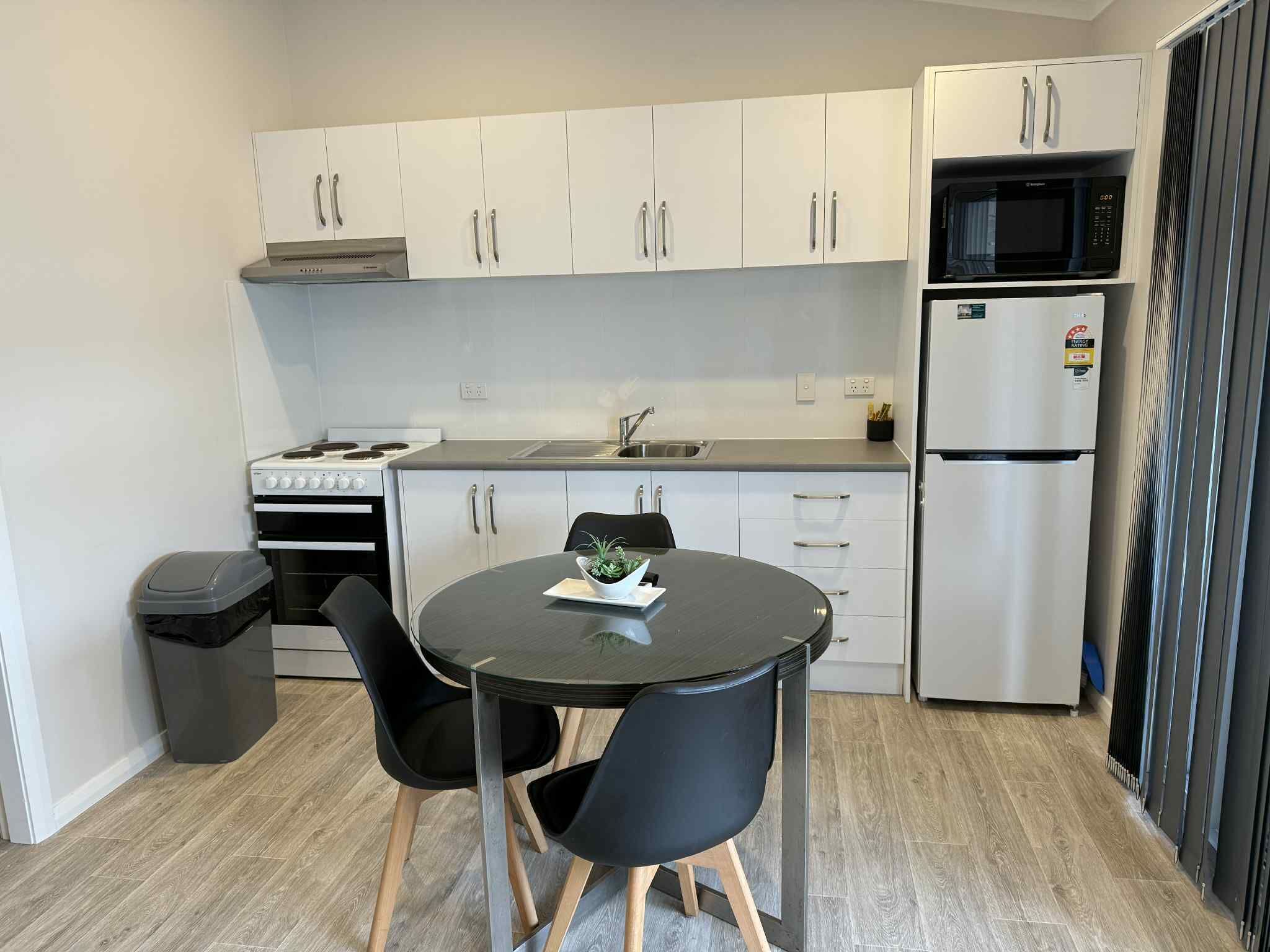 A compact kitchen with white cabinets, a microwave, a stove, and a refrigerator. There is a small dining table with two chairs.