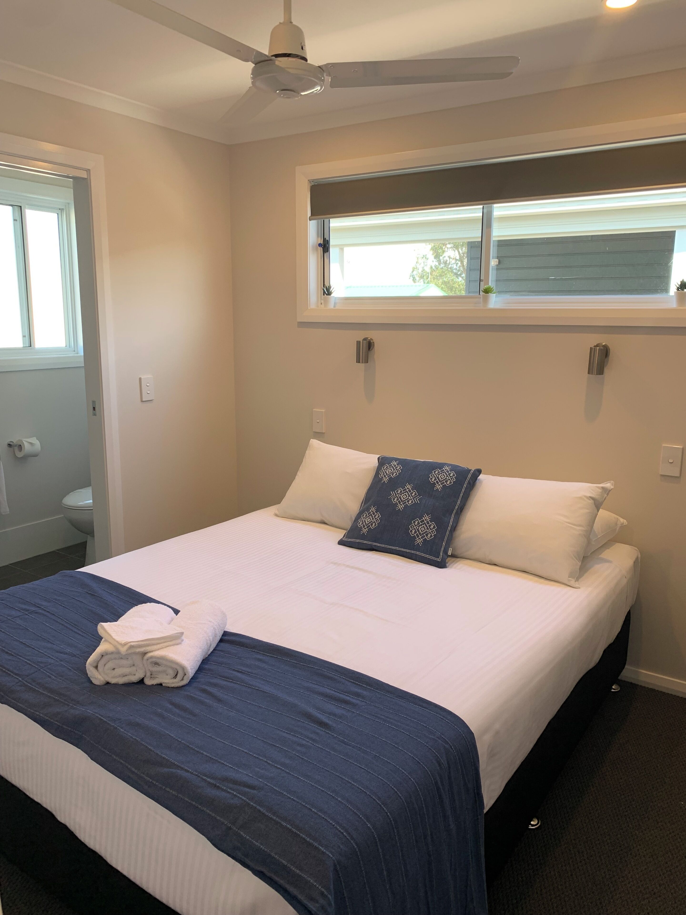 A neatly made bed with a blue and white bedspread, a rolled white towel, and a decorative pillow.