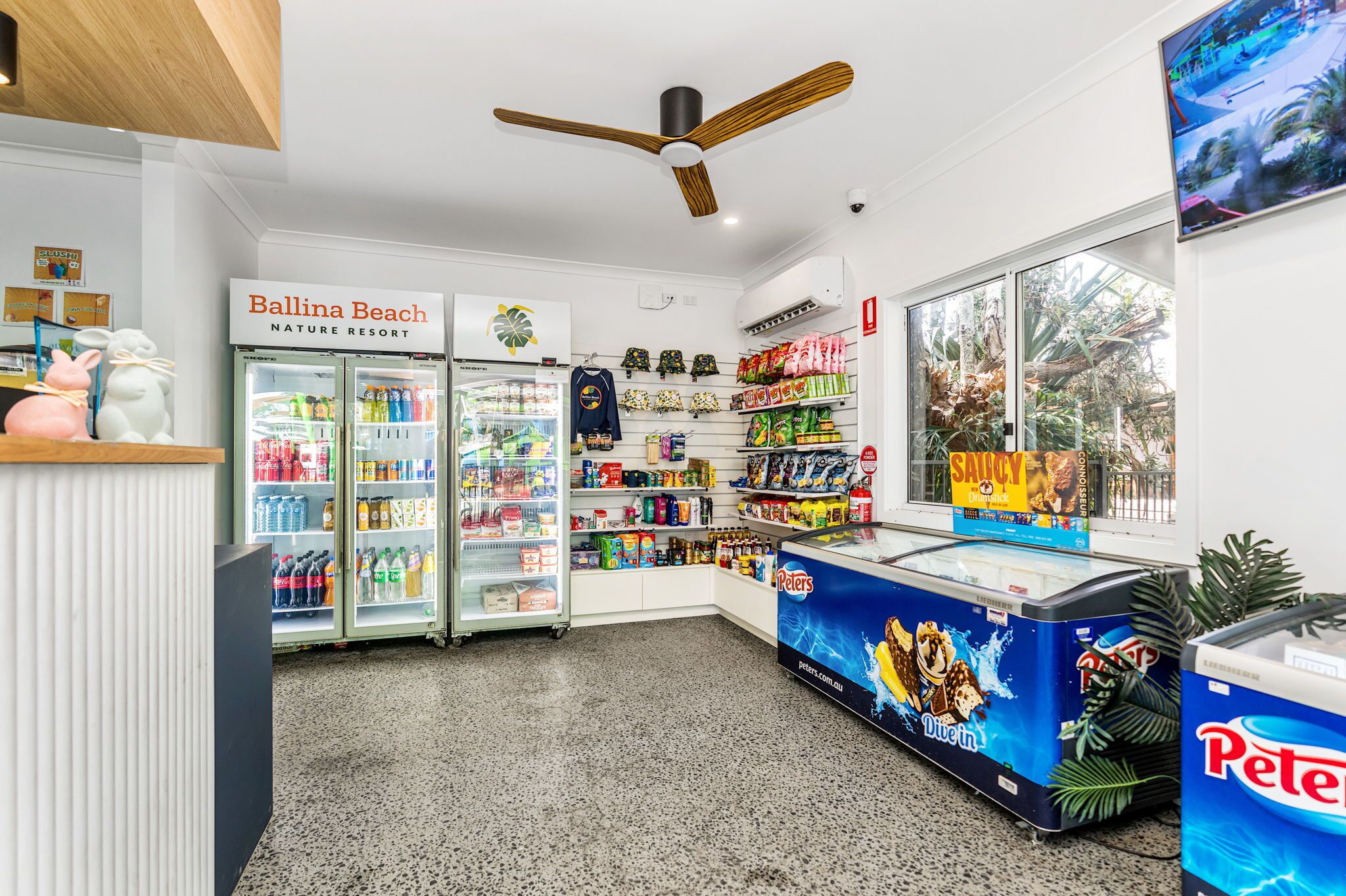 Un espace de vente au détail comprenant un présentoir réfrigéré, des étagères remplies de collations et de boissons, et une enseigne indiquant le « Ballina Beach Nature Resort ».