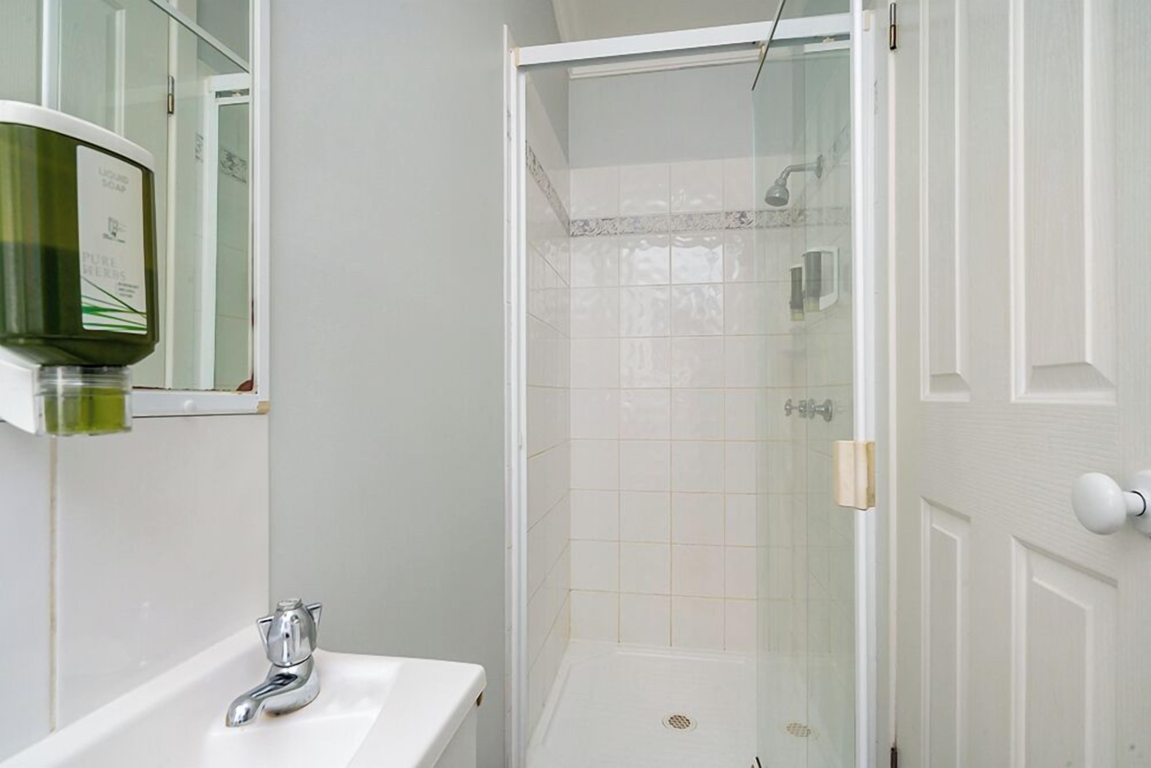 A bathroom with a white sink, a glass shower enclosure, and a soap dispenser.