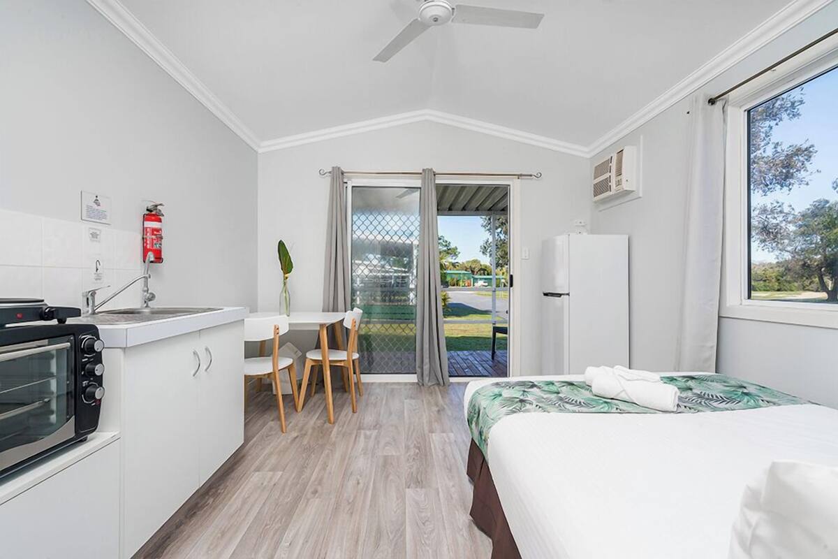 A compact hotel room with a kitchenette, a dining area, a bed, and a sliding glass door to the outside.