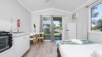 A compact hotel room with a kitchenette, a dining area, a bed, and a sliding glass door to the outside.