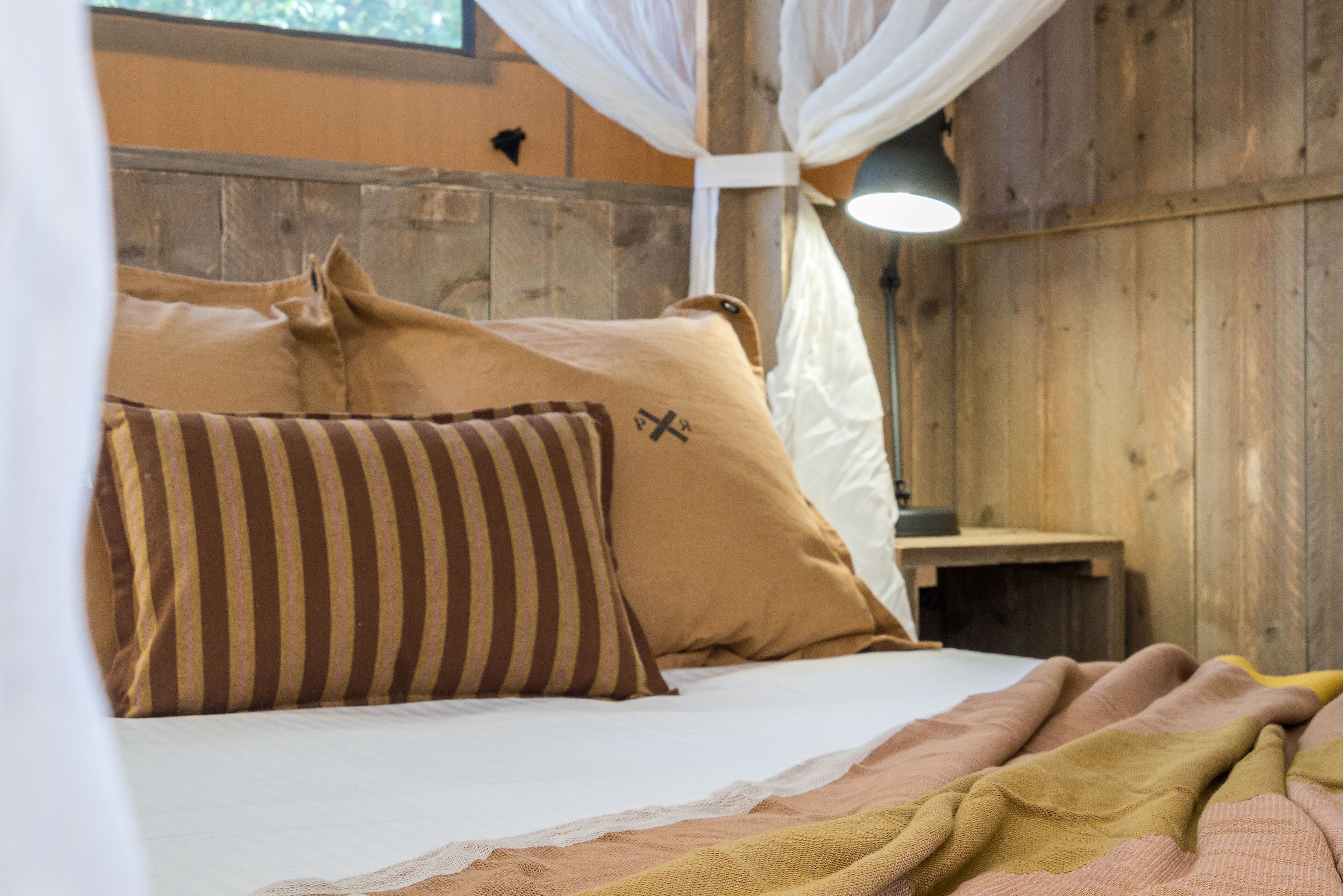 A bed with striped and plain pillows, a bedside table, and a lamp.