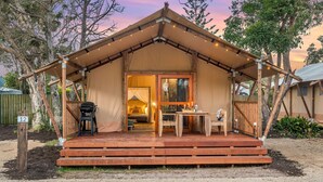 Alojamiento tipo tienda rústico con terraza de madera, zona de comedor y cama visible en su interior.