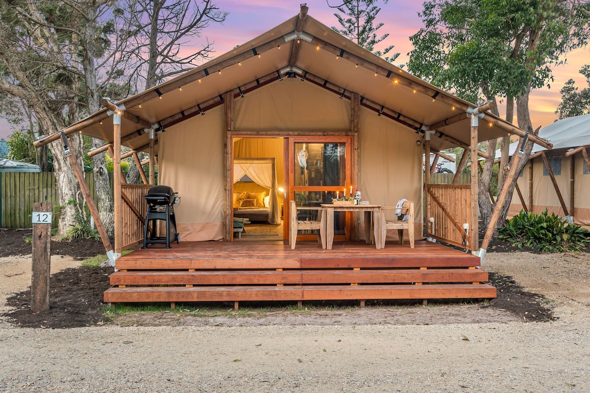 A rustic tent-style accommodation with a wooden deck, a dining area, and a visible bed inside.