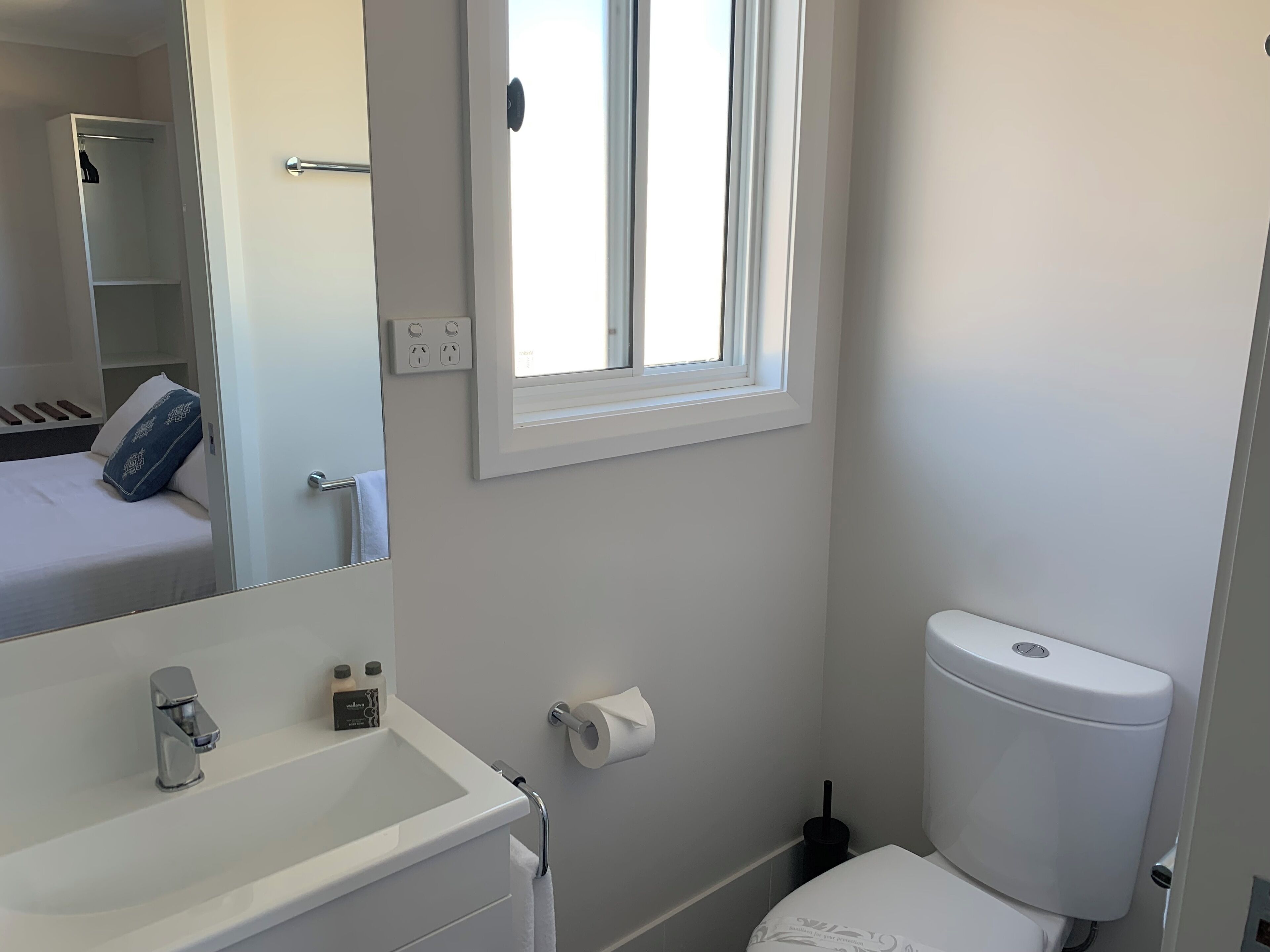 Un baño con lavamanos, inodoro y una ventana sobre el inodoro.