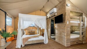 Una habitación tipo tienda de campaña con cama con dosel, una litera de madera, un televisor de pantalla plana y una planta en maceta.