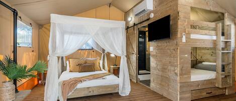 Une chambre aménagée comme une tente, avec un lit à baldaquin, un lit superposé en bois, un téléviseur à écran plat et une plante en pot.