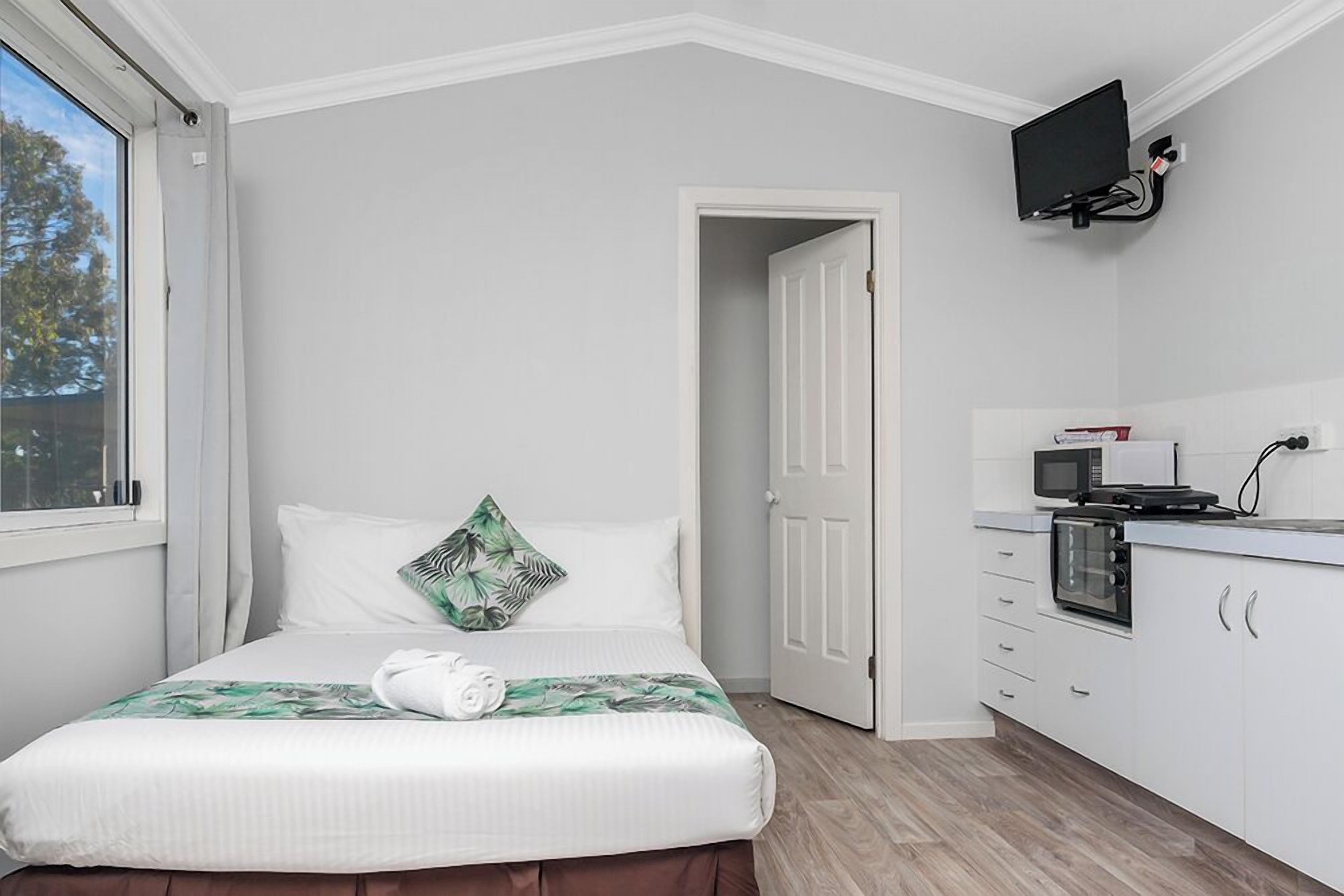 Una camera da letto con un letto, una TV fissata al muro, un forno a microonde e una porta che dà su un'altra stanza.