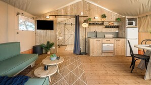Alojamiento con carpa que incluye una kitchenette, un comedor con mesa y sillas, un sofá y un televisor en la pared.