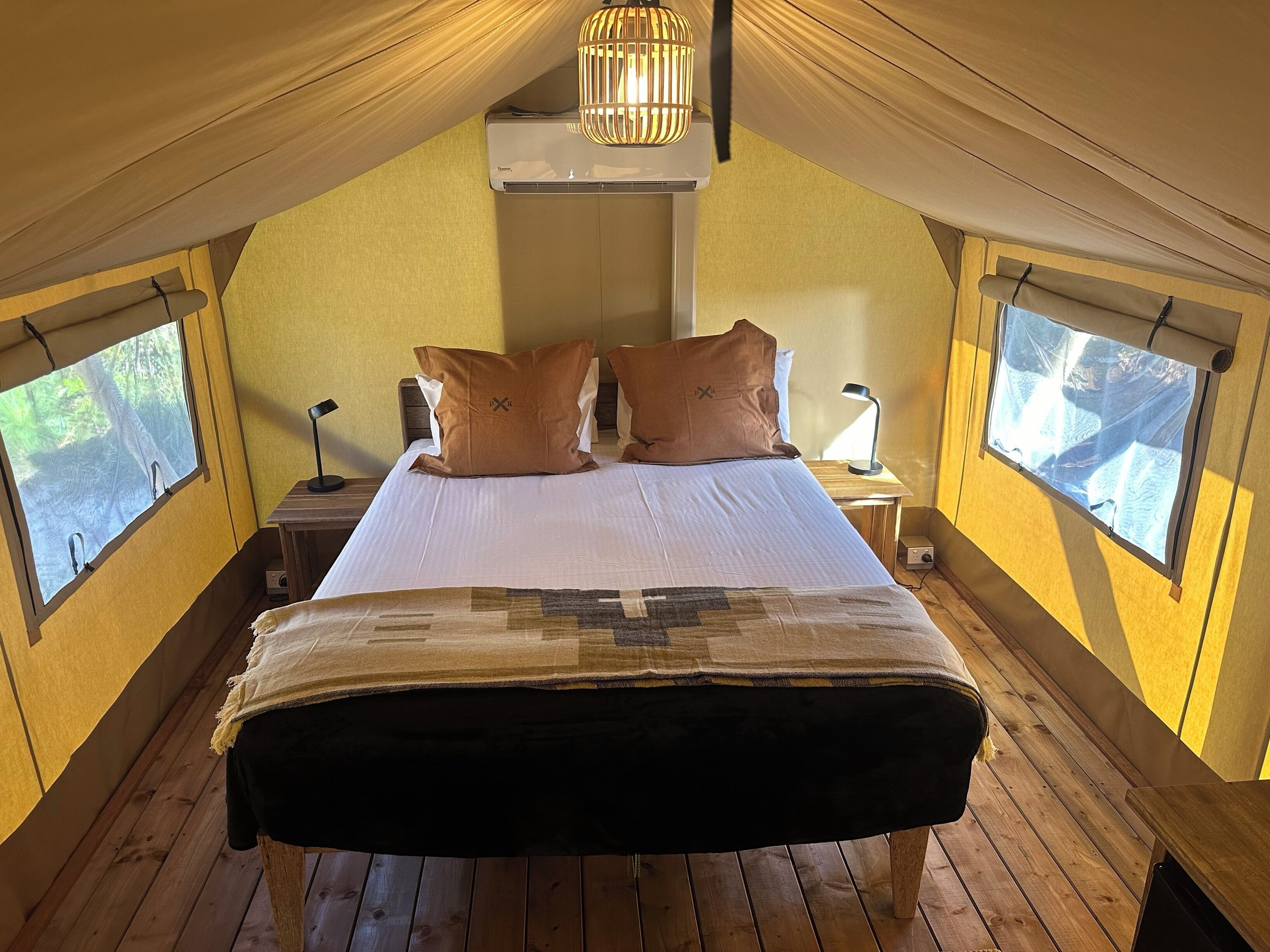 Un dormitorio cálido en el ático, con una cama grande, dos ventanas, un ventilador de techo y una lámpara colgante.