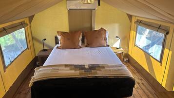 Un dormitorio cálido en el ático, con una cama grande, dos ventanas, un ventilador de techo y una lámpara colgante.