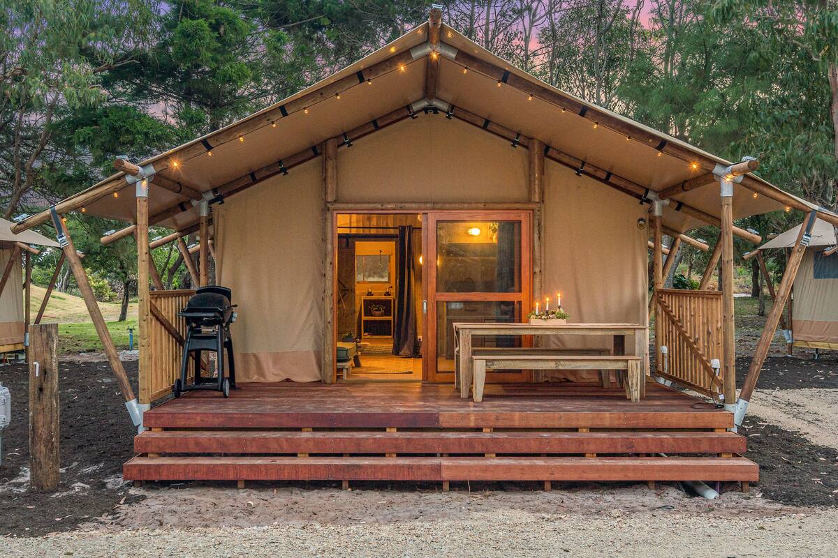 A rustic wooden tent with a covered porch, a table, and a bench.