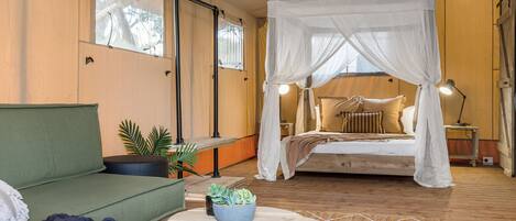 A bedroom with a canopy bed, a green sofa, a small table with a plant, and a bedside lamp.