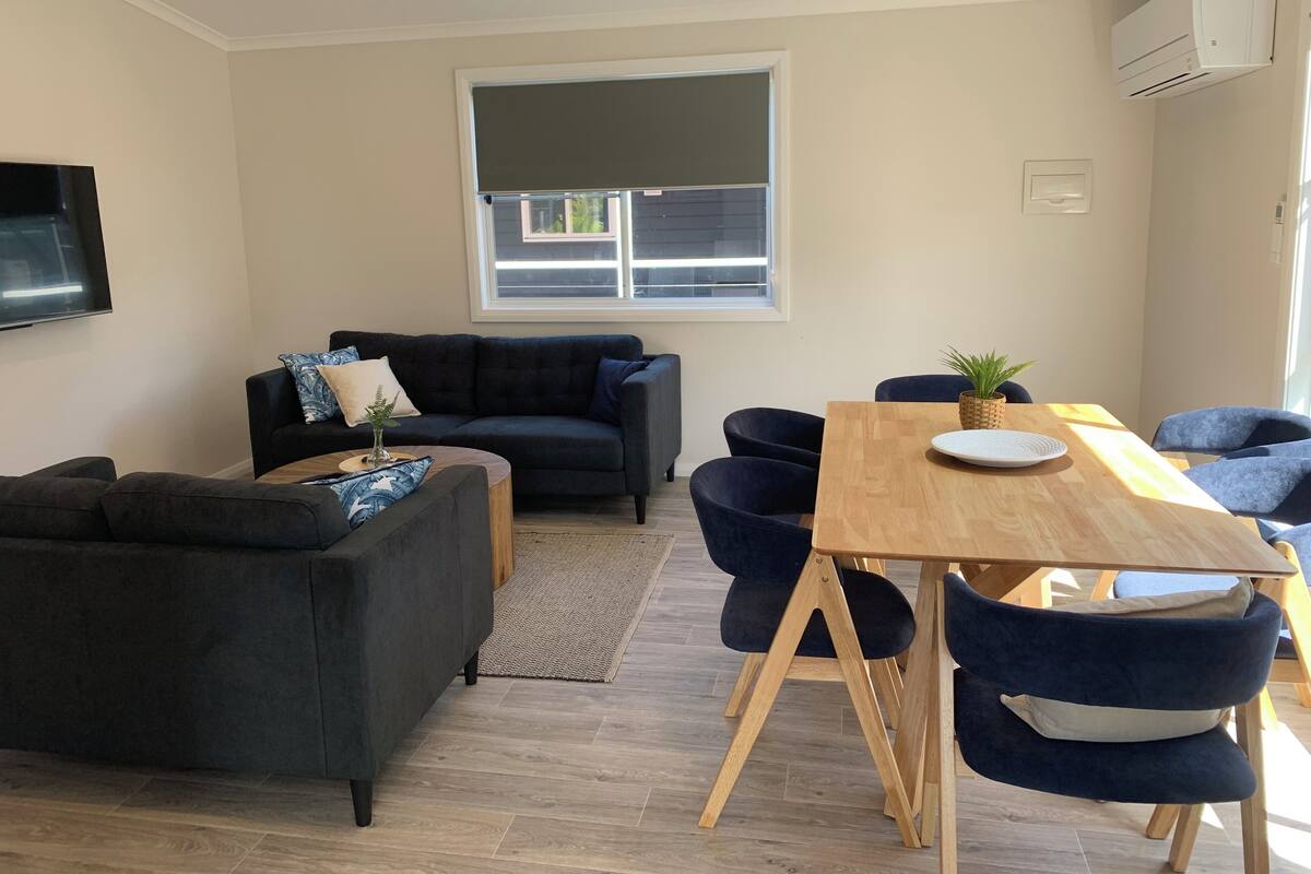 A modern living room with a dark-colored sofa, a wooden dining table, and blue chairs.