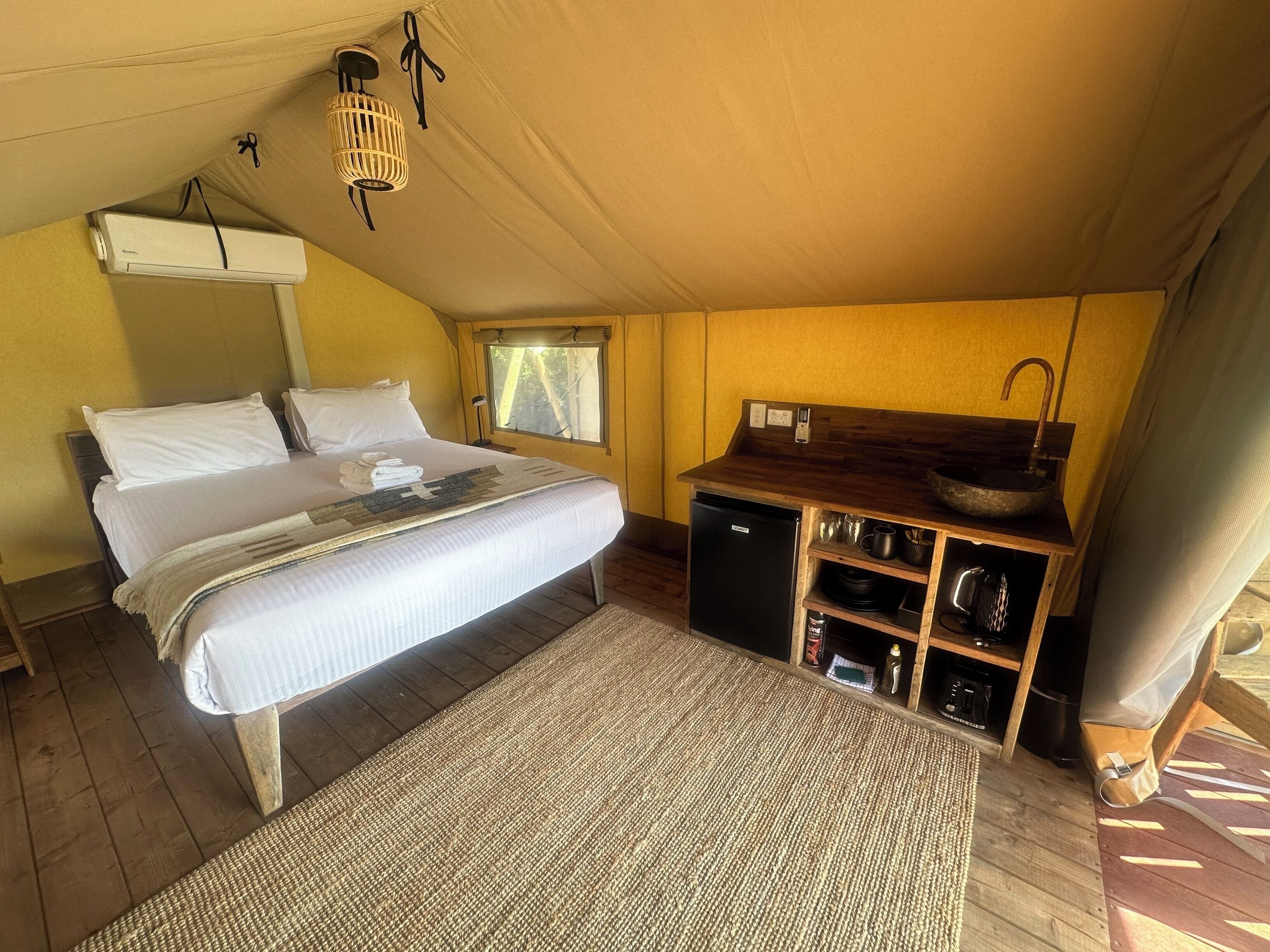A bedroom with a bed, a small kitchenette, a window, and a ceiling fan.