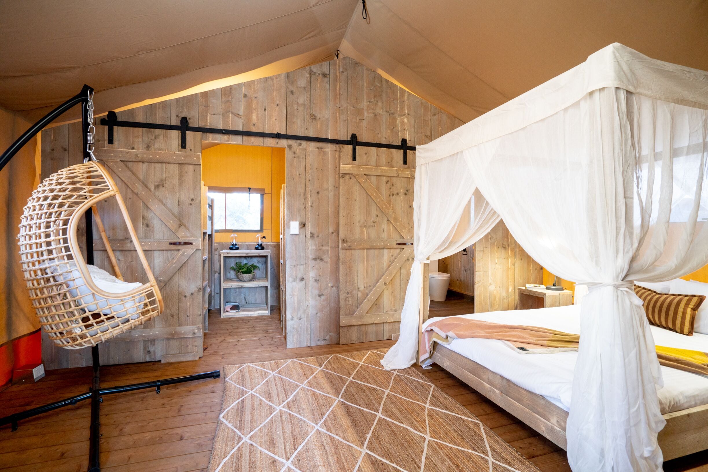 A bedroom with a canopy bed, a hanging chair, and a wooden floor.