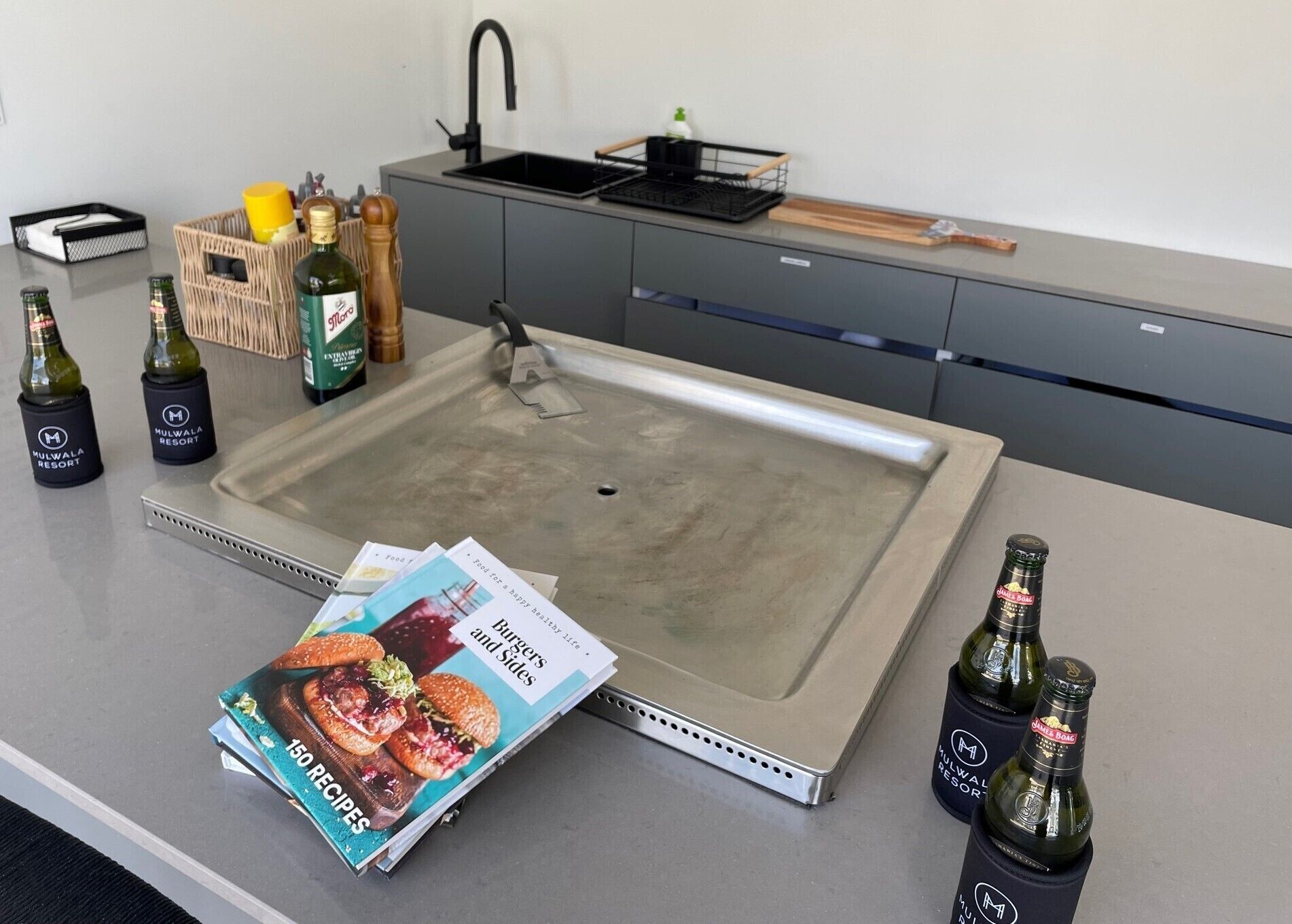 Una cocina con un lavamanos de acero inoxidable, una revista y botellas de cerveza.