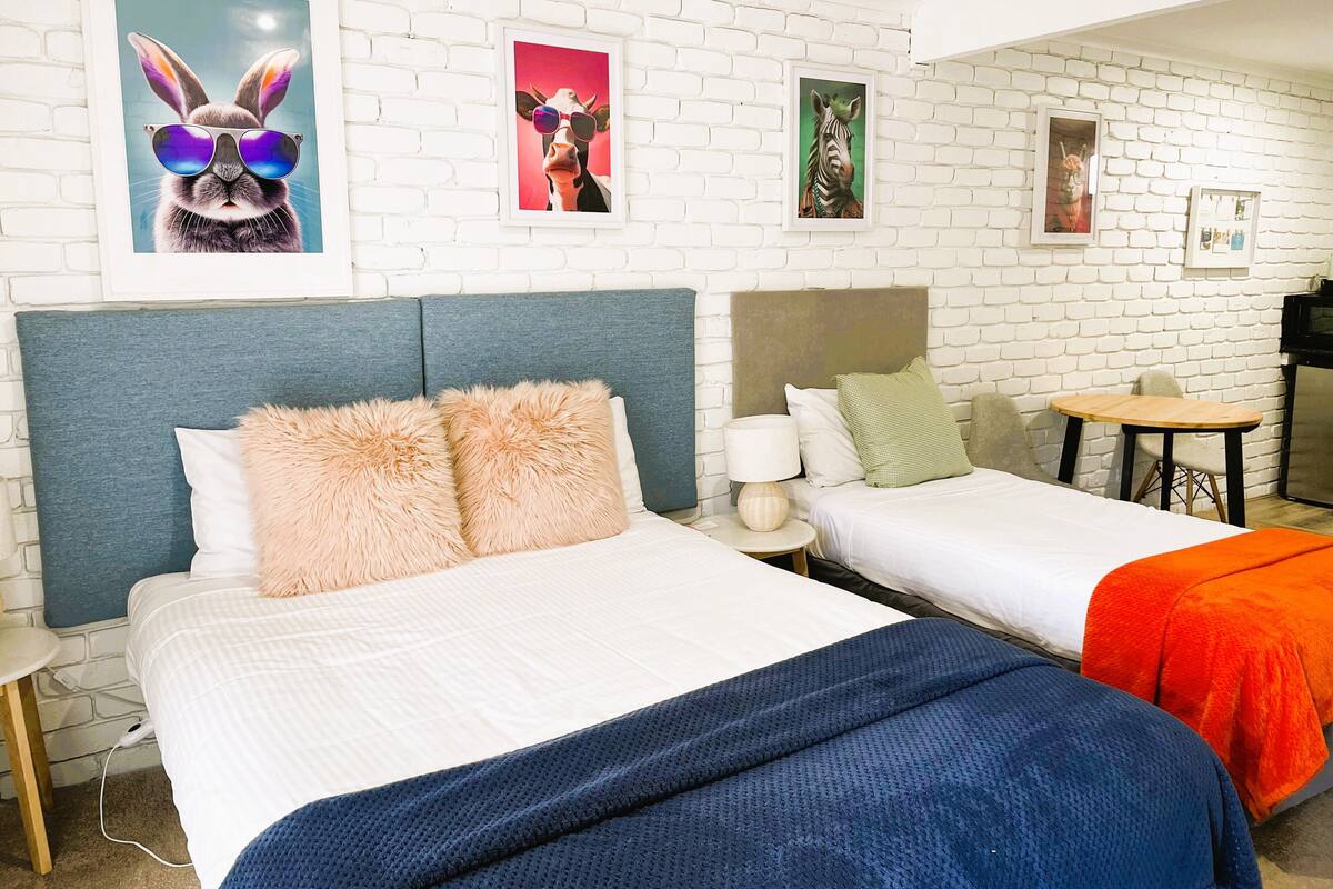 A hotel room with two beds, a small table, and a chair. There are framed pictures on the wall.