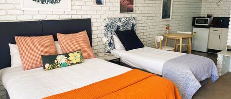 A hotel room with two beds, a small kitchenette, and a dining area.
