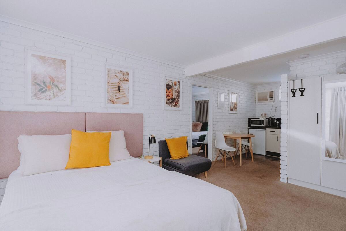 A hotel room with a bed, a desk, a chair, a wardrobe, and a kitchenette.