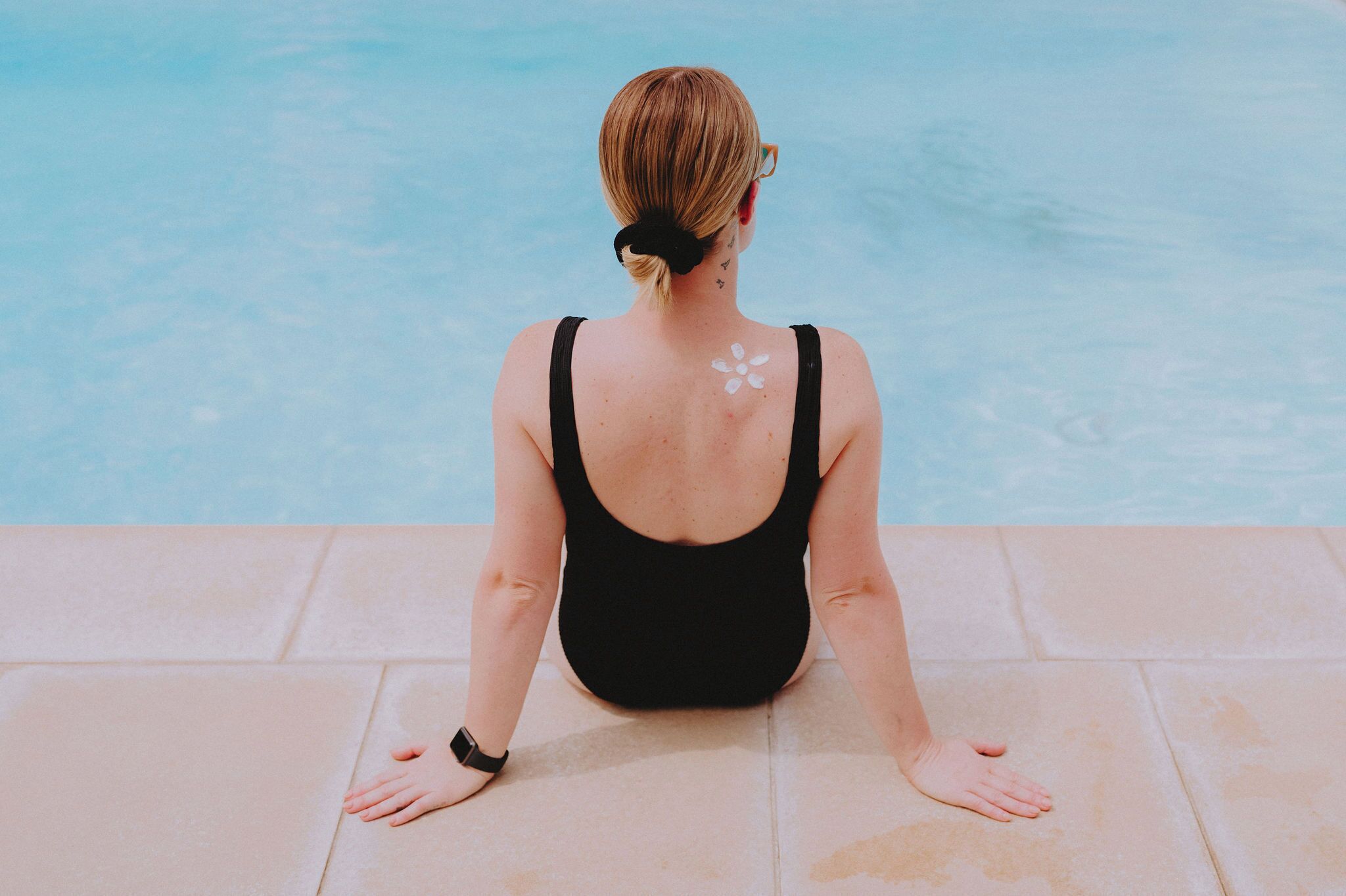 A person sitting by a pool with a back tattoo and a flower design.