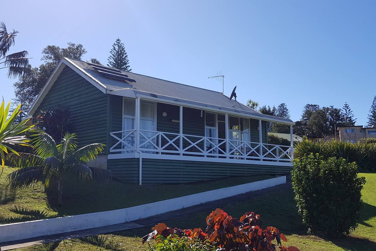 A single-story house with a balcony, surrounded by a well-maintained lawn and palm trees.