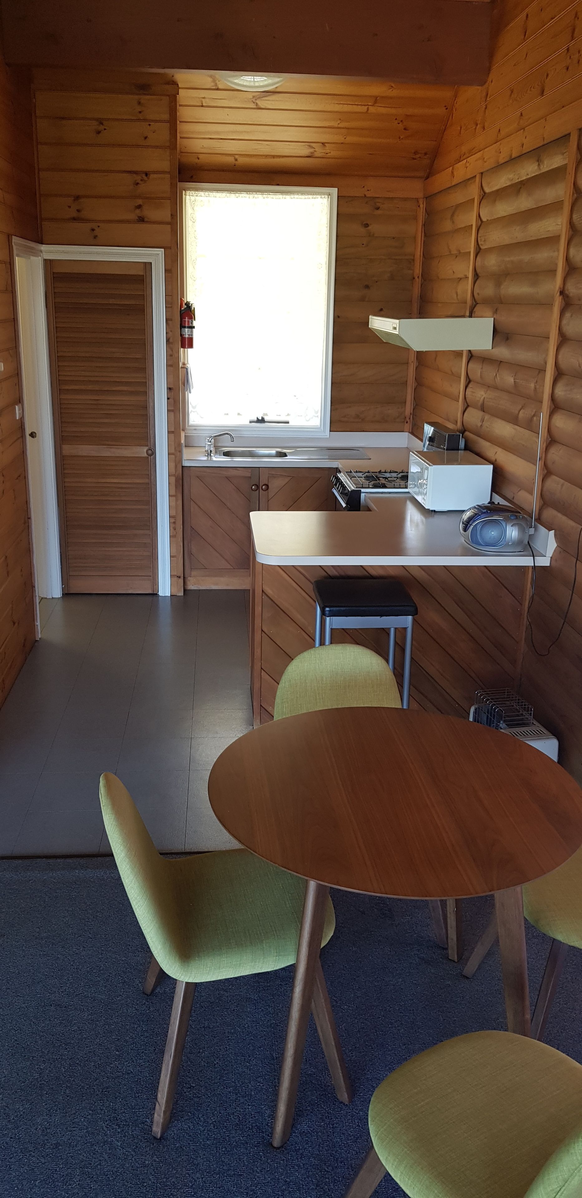 Una cabaña de madera acogedora con kitchenette, un comedor con dos sillas y un ventanal que proporciona luz natural.