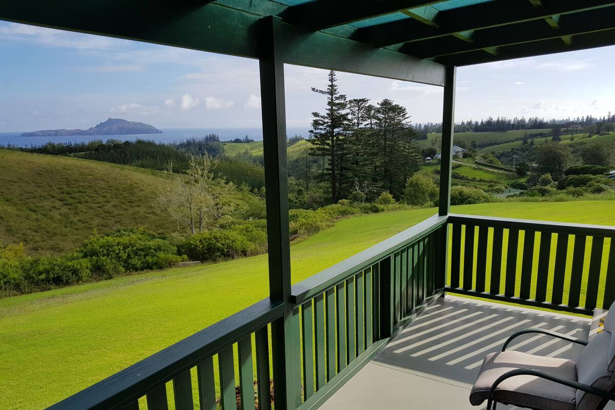 A covered balcony with a view of a green landscape and distant mountains.