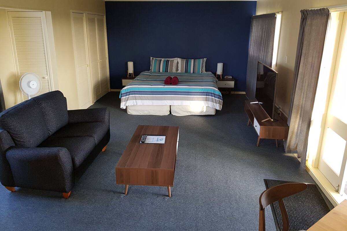 A hotel room with a bed, a sofa, a coffee table, a TV, and a fan.