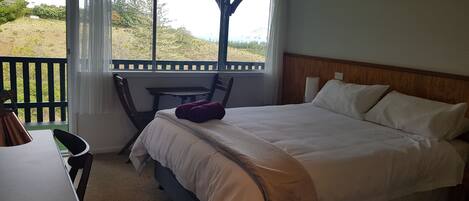 A bedroom with a bed, a desk, and a chair. There is a window with a view of the outdoors.