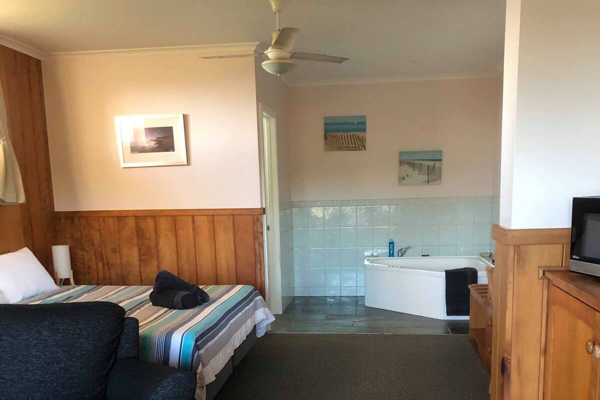 A hotel room with a bed, a sofa, a TV, a desk, and a bathroom with a bathtub and shower.