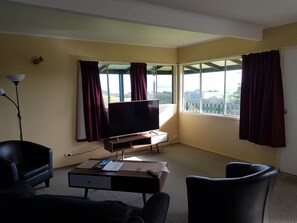 A room with a TV on a stand, a desk with a chair, and a large window with curtains.