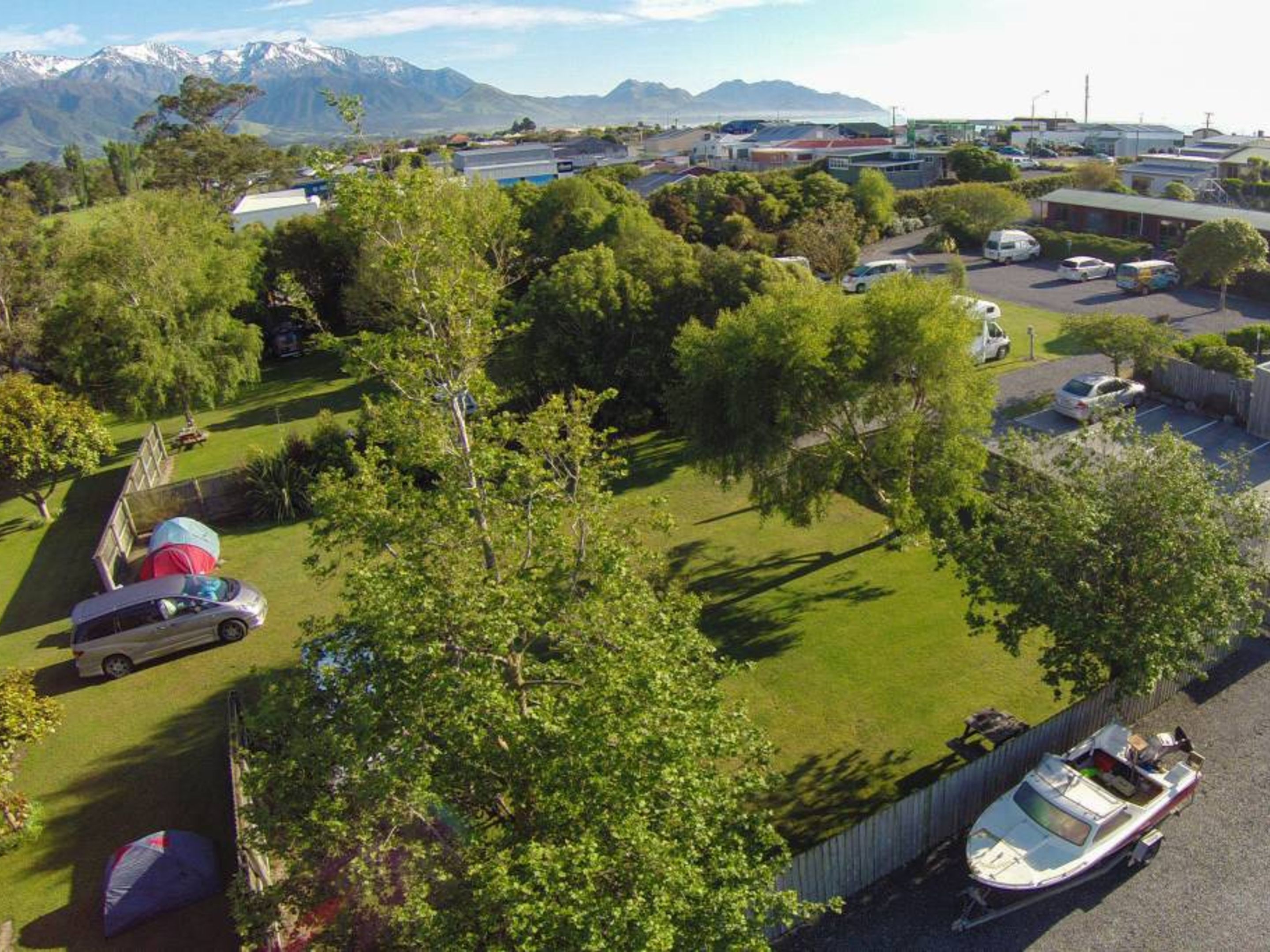 A residential area with a boat docked near a house, surrounded by trees and a mountainous backdrop.